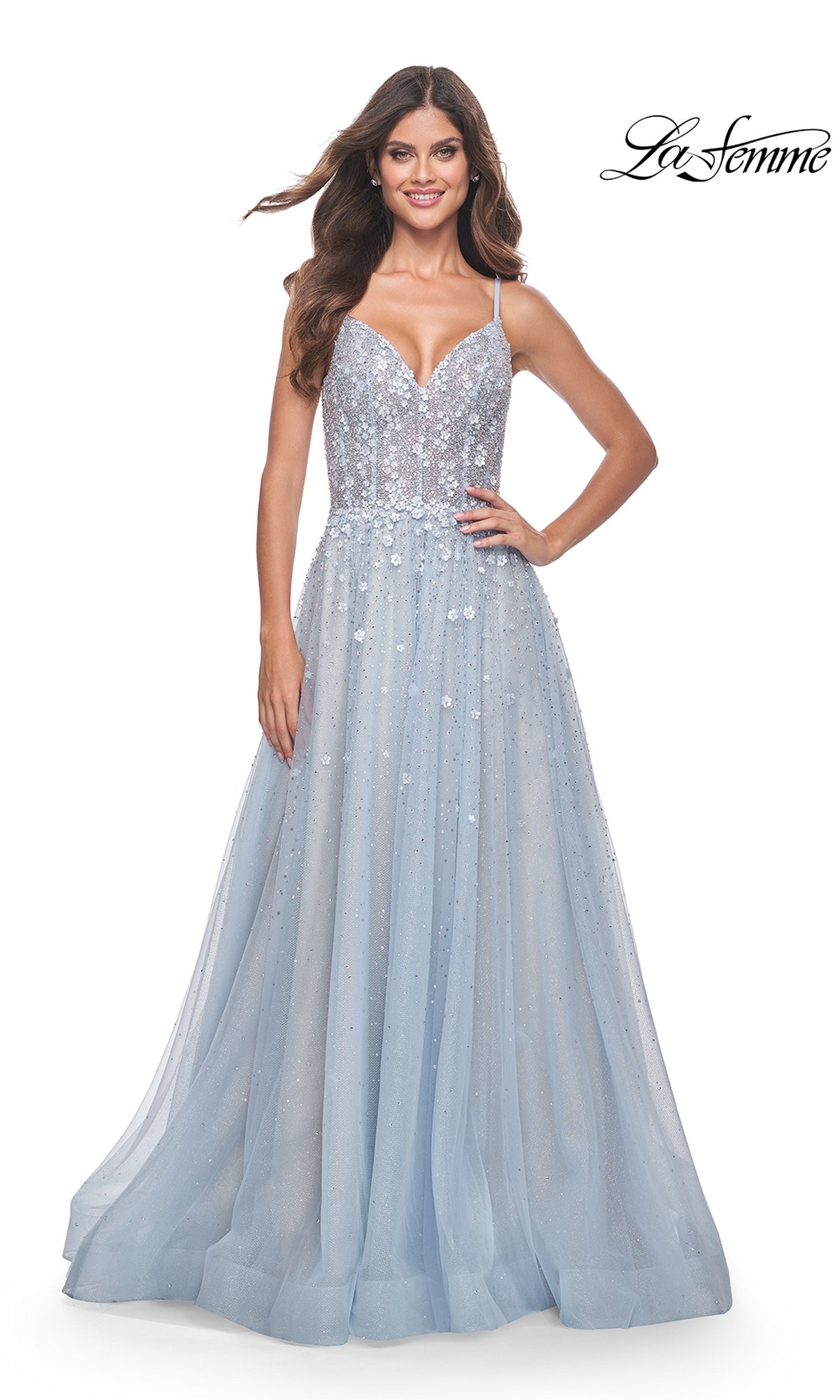 A woman wears the La Femme Embellished Long A-Line Prom Dress 32215, featuring sequins, thin straps, and a flowing light blue tulle skirt, while standing against a plain white background.